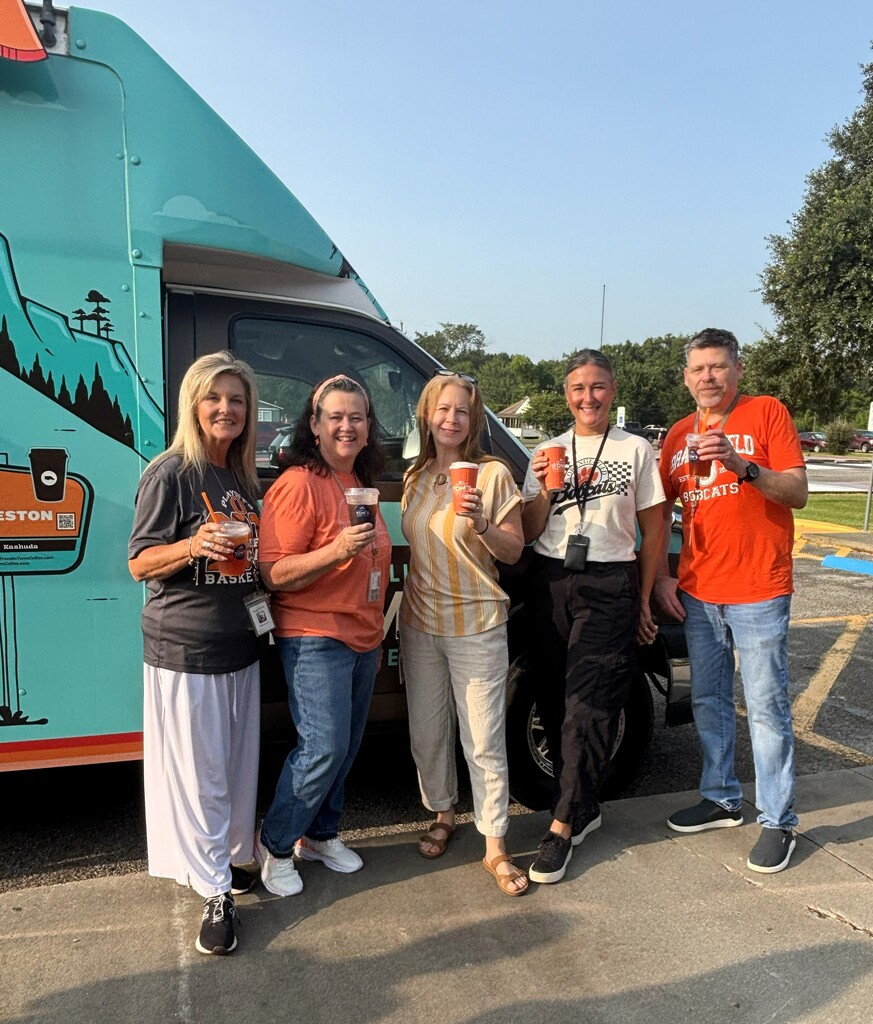 Five people in a parking lot holding cups, posing in front of a blue truck.