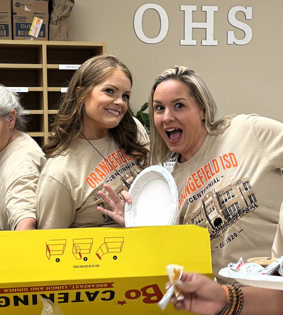 Three women in matching beige t-shirts stand beside a yellow box labeled Bojangles. One woman holds a white plate.