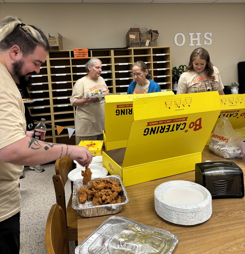 A group of people in a room with shelves in the background, serving food from a yellow box.