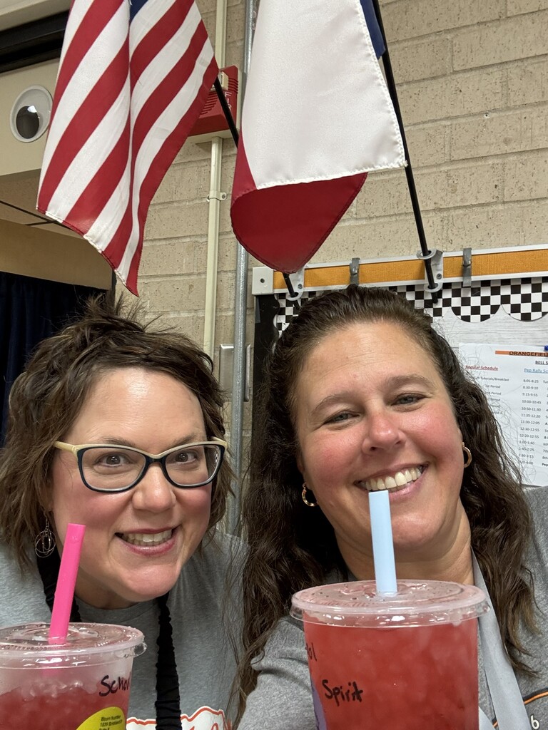 Two women smiling, holding drinks with straws; flags of USA and Texas in the background.