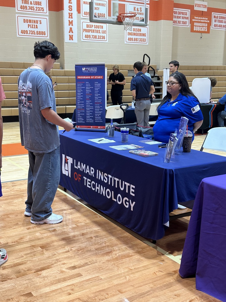 People stand near a table covered in a blue cloth. One person wears a blue shirt with "Lamar Institute of Technology" printed on it.