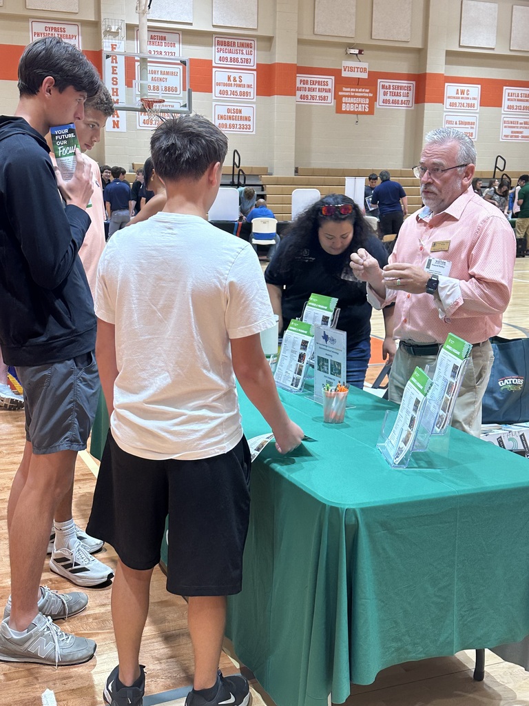 People stand around a table with green cloth, with one man speaking to a woman and two men looking at a display.