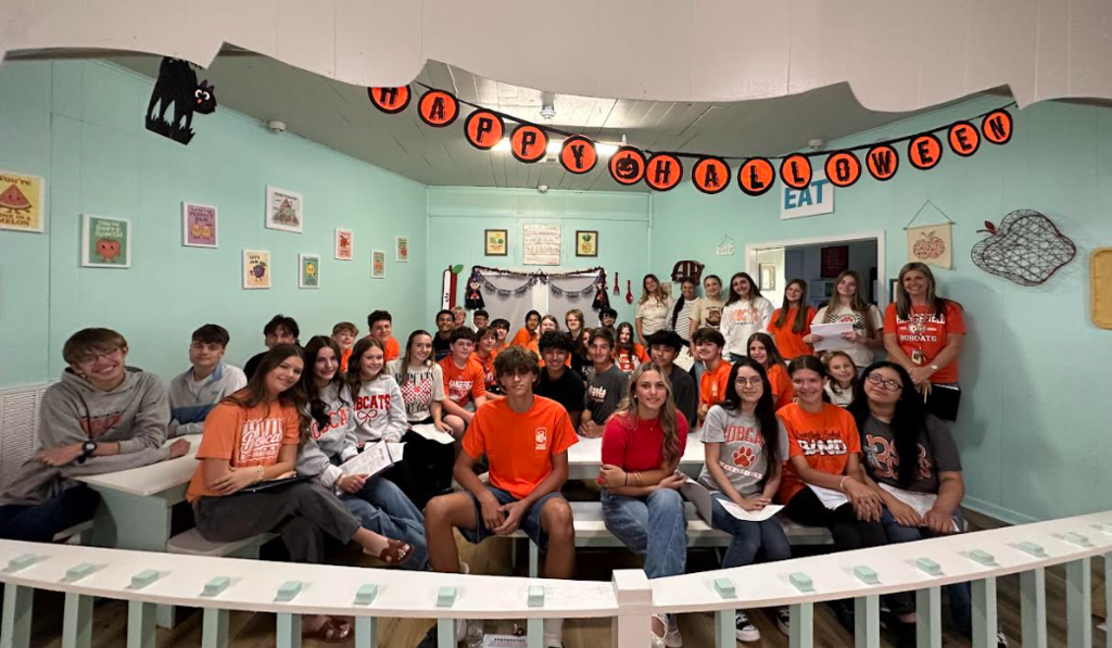 A group of people in orange shirts pose for a photo in a room decorated with Halloween items.