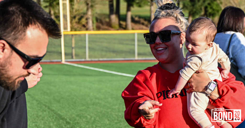 Woman holding baby and smiling, pointing at the camera