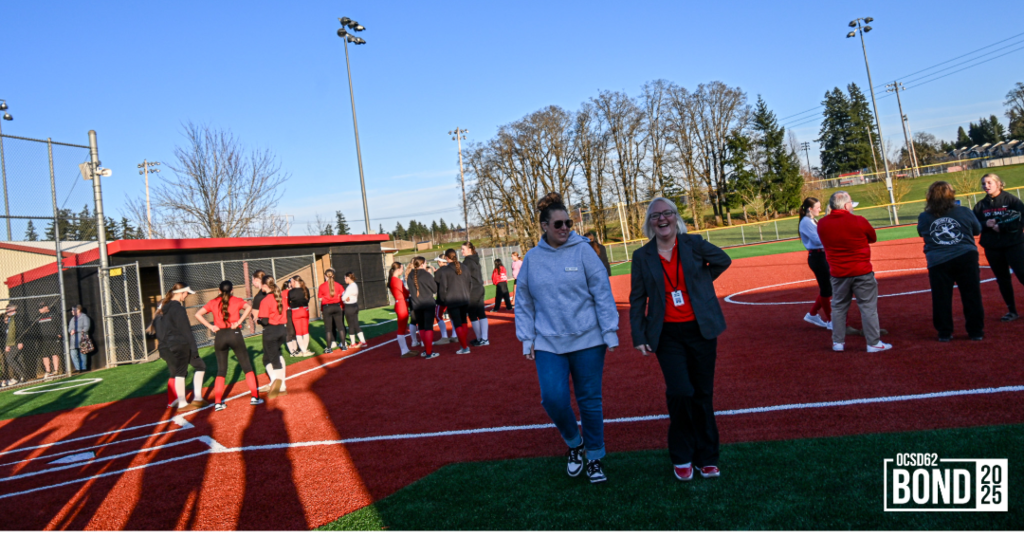 Community members and softball players smiling and standing casually on new turf surface. 