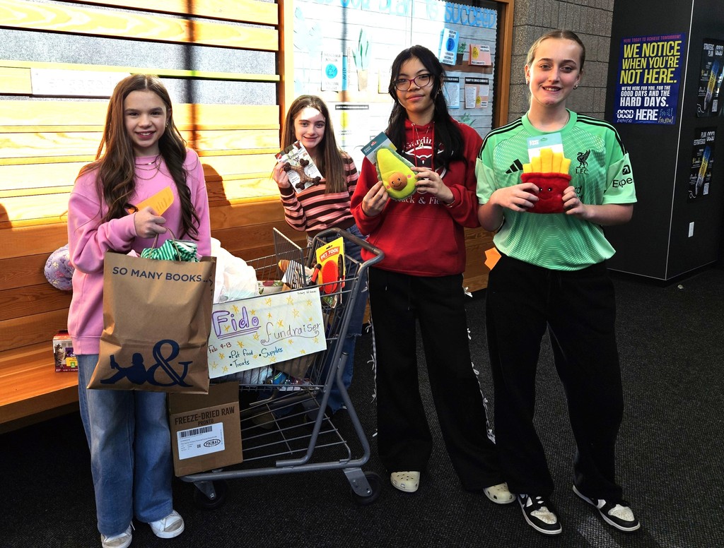 Four girls holding  dog toys and standing with a cart filled with pet supplies for the FIDO fundraiser.