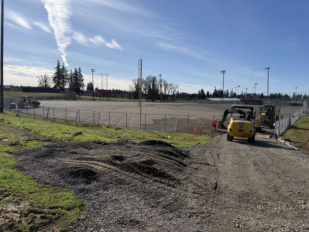 OCHS Varsity Baseball field being prepped for turf surface installation, gravel has been pressed flat and construction vehicles are in the foreground.