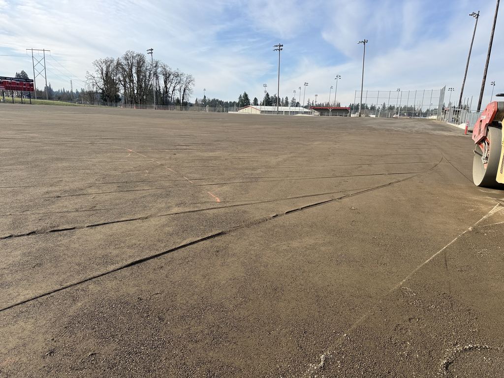 OCHS Varsity Baseball field being prepped for turf surface installation, gravel has been pressed flat and a roller machine shows at the edge of the field.