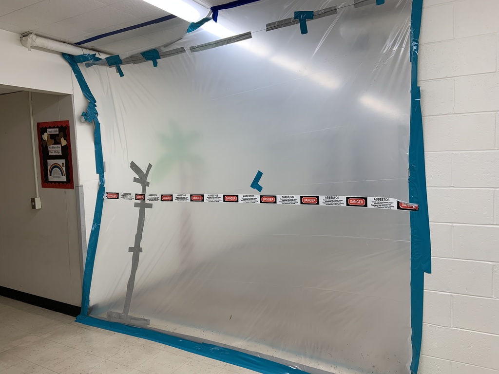 Large protective barrier wall constructed of plastic sheeting secured with blue tape and lined with asbestos warning signs.