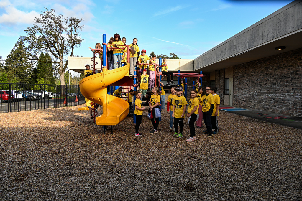 A group of students wearing yellow shirts that say "No Place for Hate", gathered on a play structure posing for a photo
