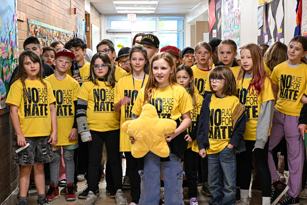 A girl holding a plush star standing in front of a group of students wearing yellow shirts that say "No Place for Hate"