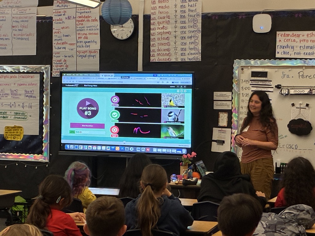 Teacher Carina sharing information about bird and their songs standing in front of a classroom of students