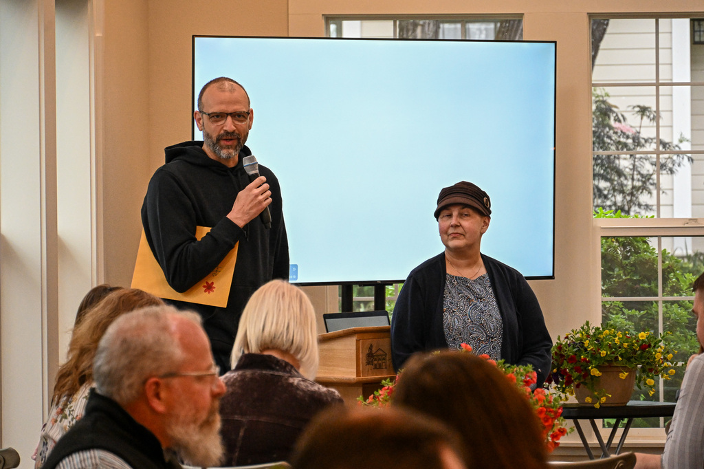 Man holding microphone while a woman stands nearby smiling