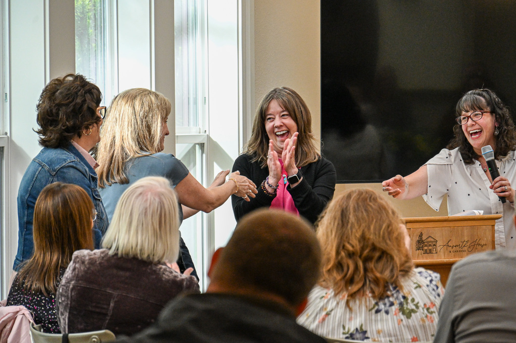 Woman smiling and clapping while three other women are standing nearby also smiling
