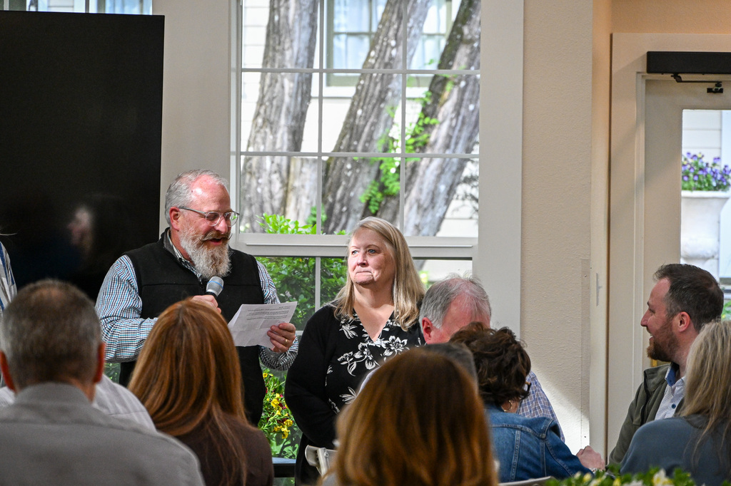 Man holding microphone reading off a paper while a woman stands nearby smiling