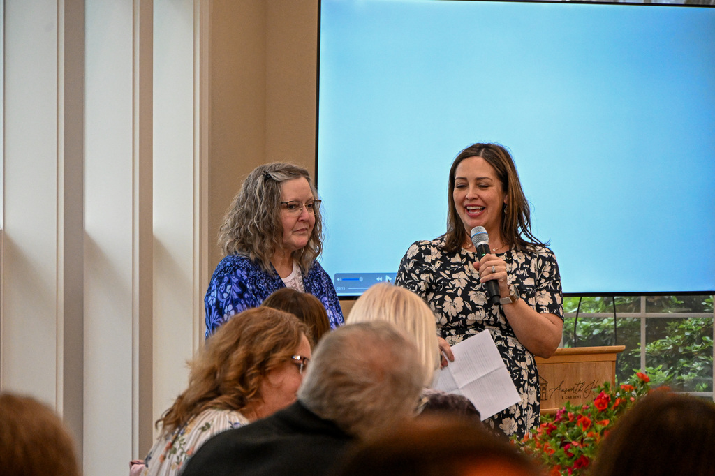 Woman, smiling, holding a microphone standing next to a woman 