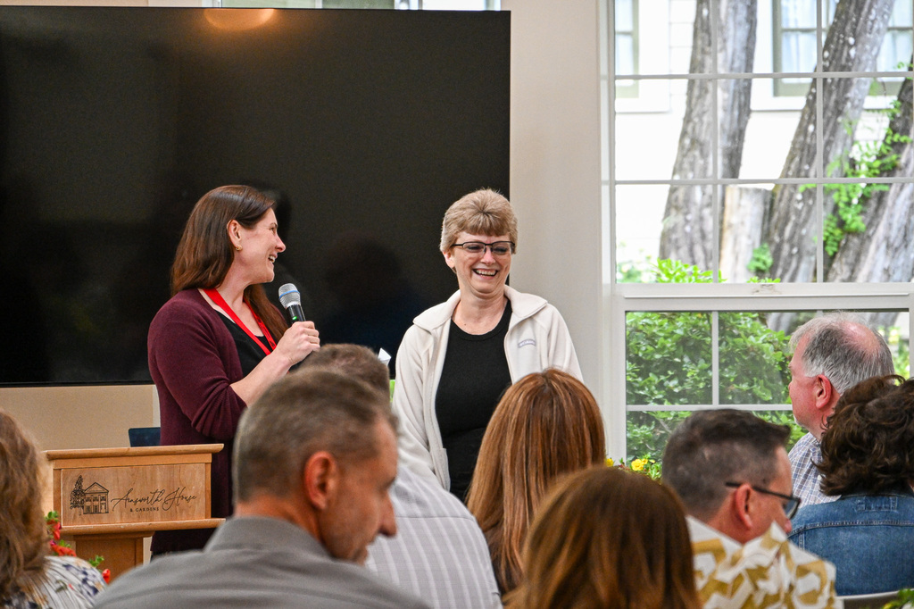 Woman, smiling, holding a microphone standing next to a woman smiling