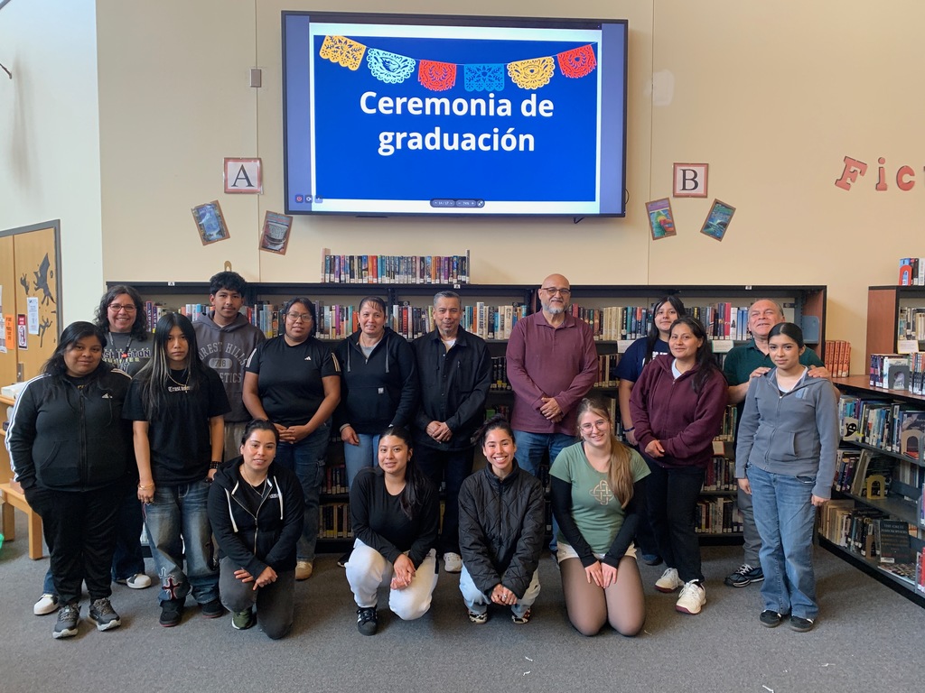 Families and their students pose in rows with "Ceremonia de graduación" on a sign above. 