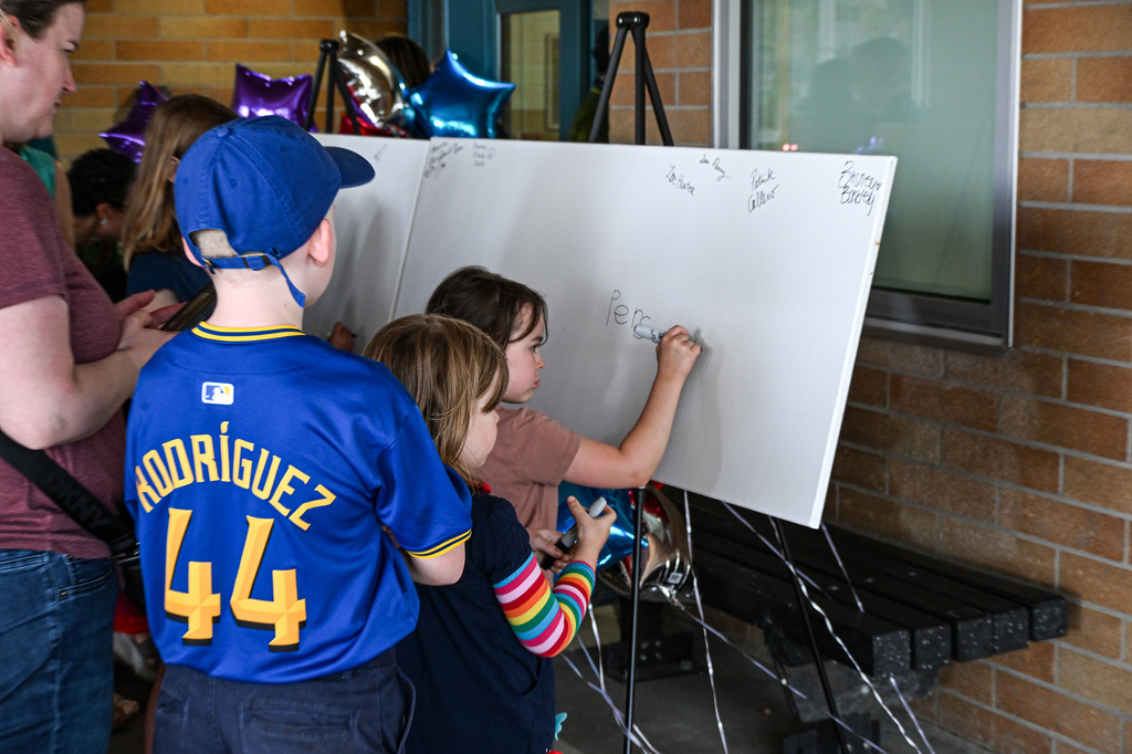 Three Candy Lane students carefully write their names with markers on a large white time-capsule board.