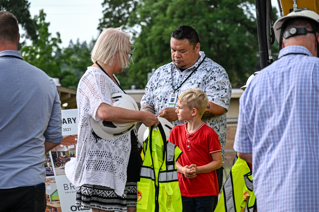 A Candy Lane student in a red shirt is fitted with a hard hat and safety vest beside a rendering of the new school's design.