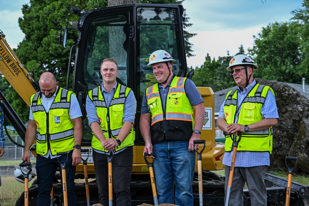 District and bond team members in safety vests and hard hats stand with ceremonial shovels in front of an excavator at the Candy Lane groundbreaking.