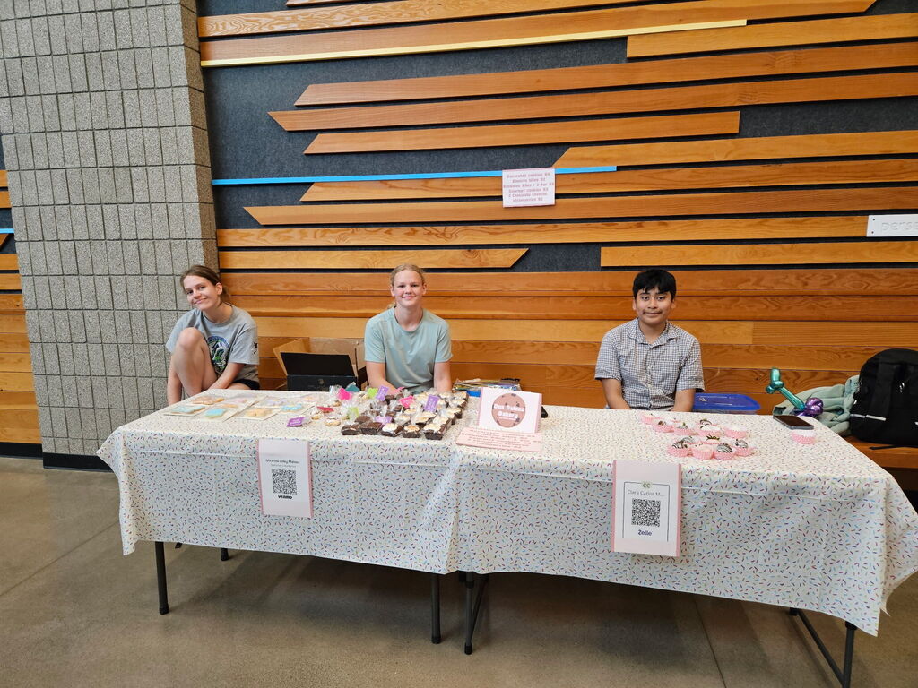 students sitting behind tables of cookies and brownies