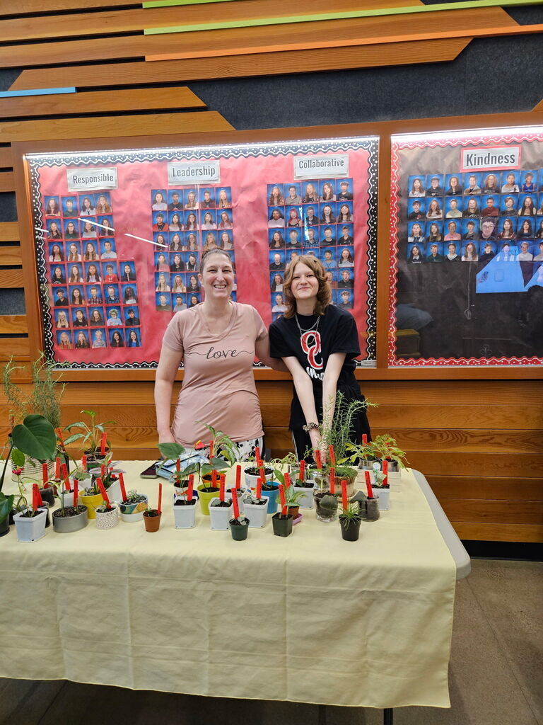 Photo of 2 ladies standing behind a table with plants on it.