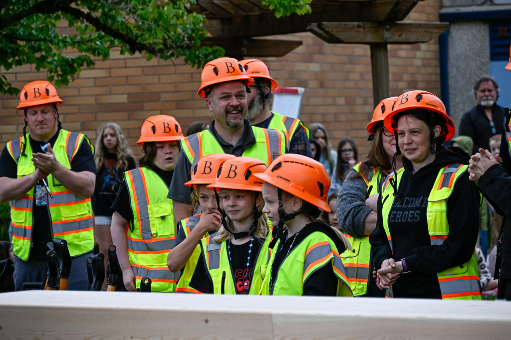 Mix of staff, community members, and students standing smiling wearing vests and hard hats. 