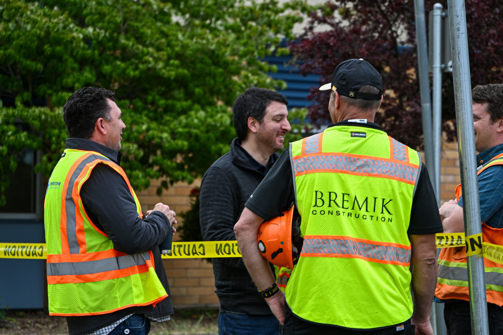 Individuals in yellow safety vests and orange hard hats stand in a group smiling and talking
