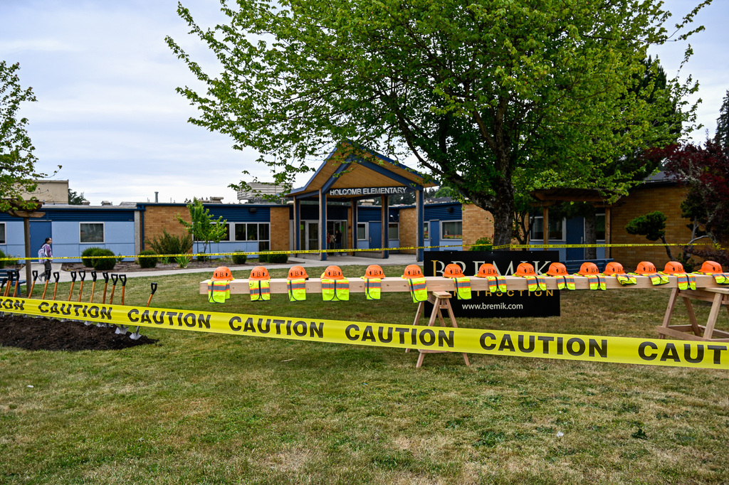 Front entrance of Holcomb Elementary with a beam in the center of yellow caution tap with hats and vests resting atop it on the front lawn. 