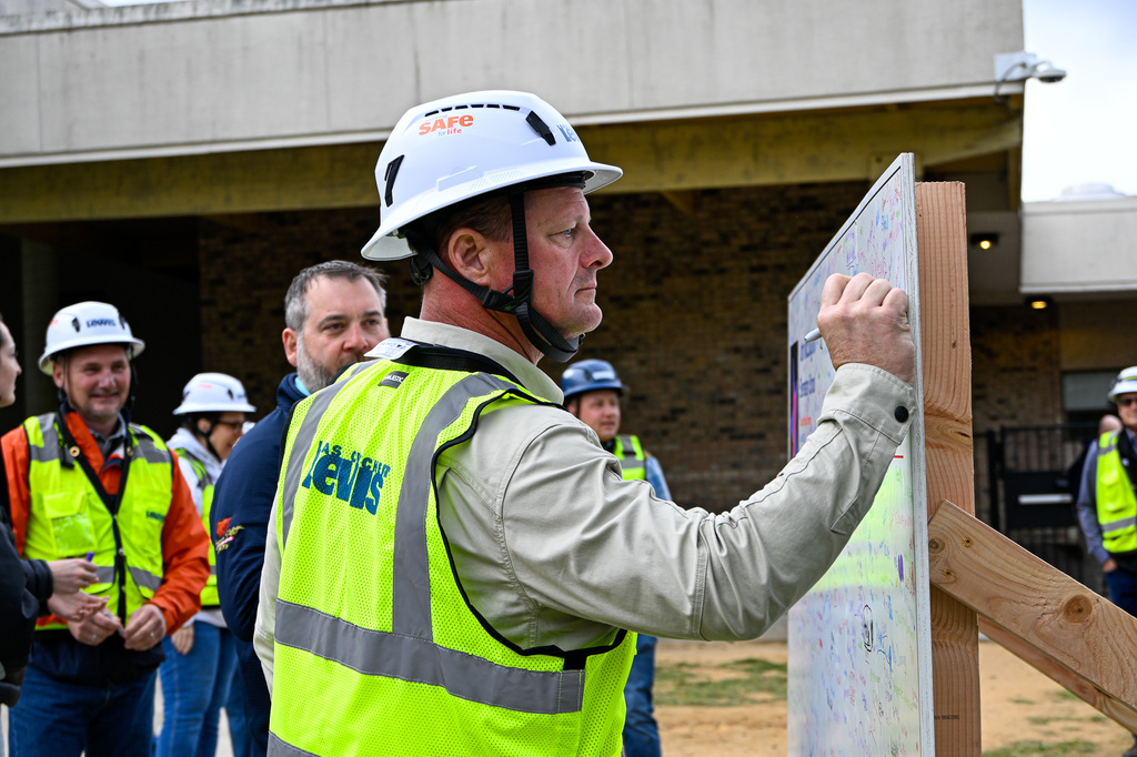 Man in hard hat and vest signing a board