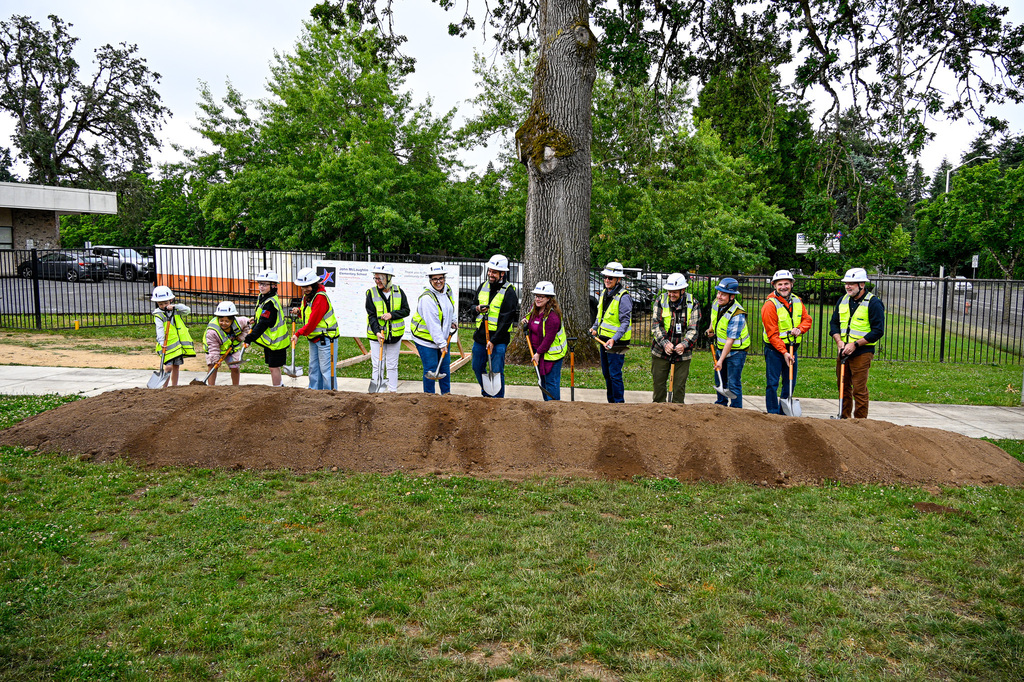 A row of people with shovels tossing dirt from a pile directly in front of them