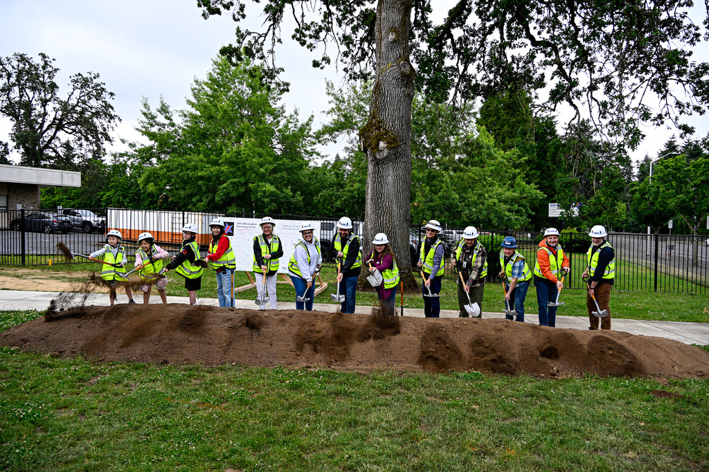 A row of people with shovels tossing dirt from a pile directly in front of them