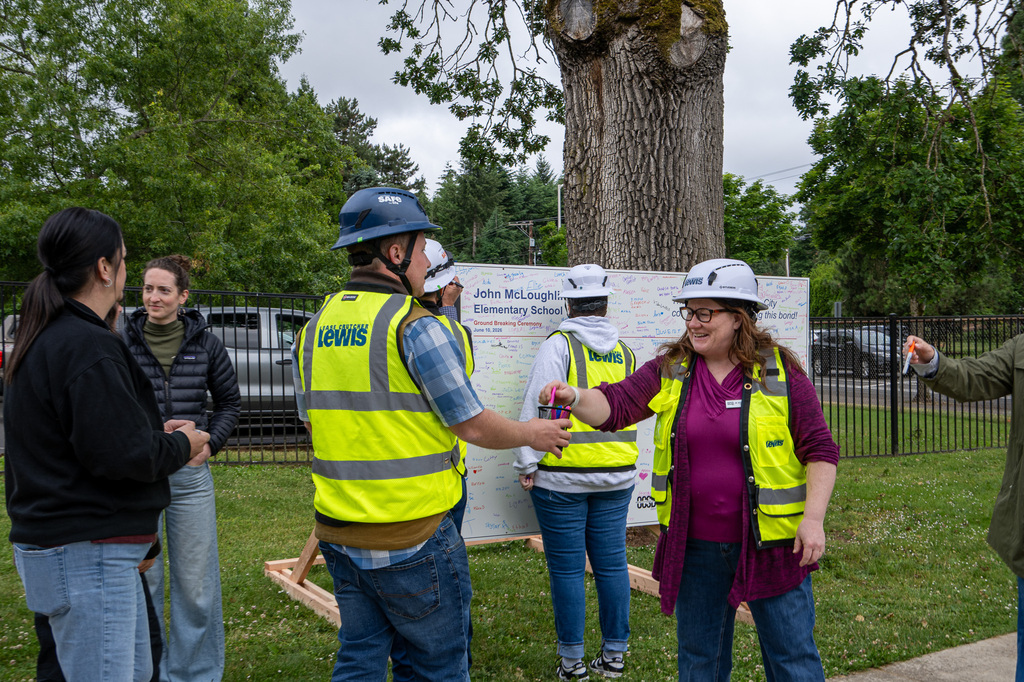 Two people in hard hats and vests, one placing a pen into a cup held by the other