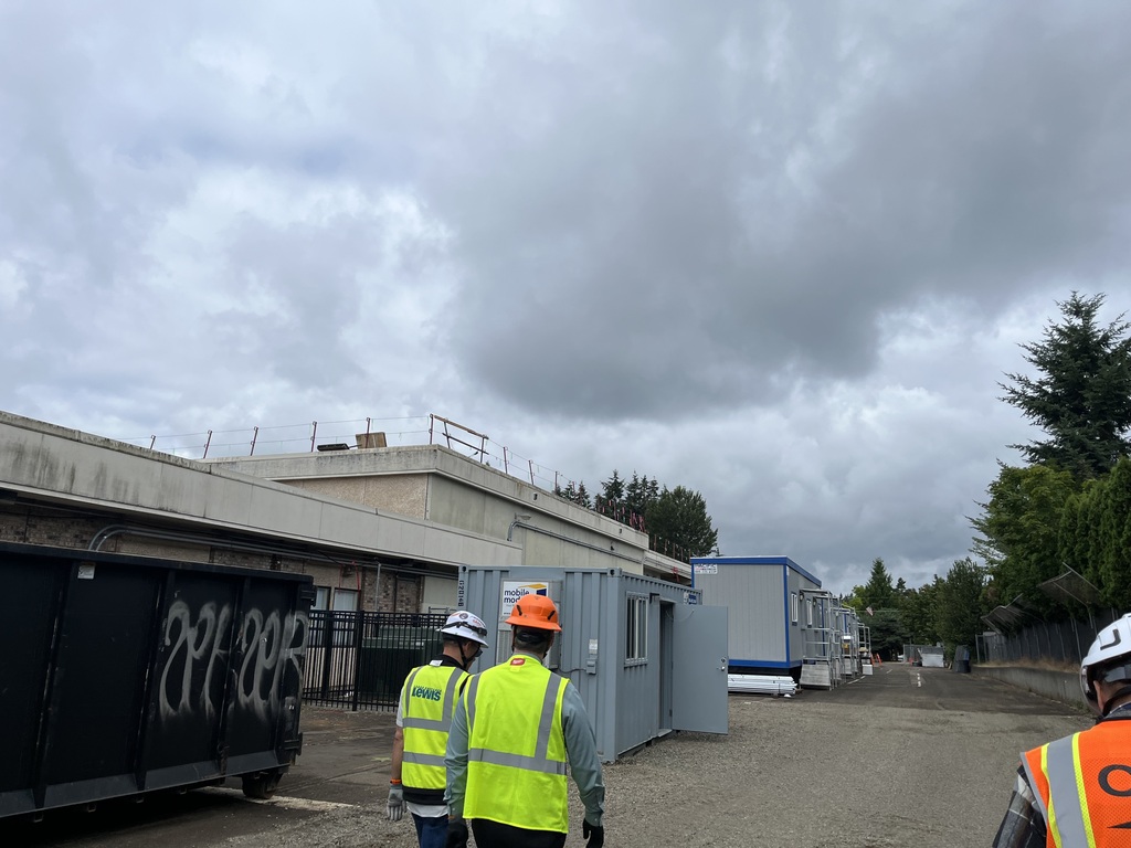 Three people wearing hard hats walking in front of construction modulars.