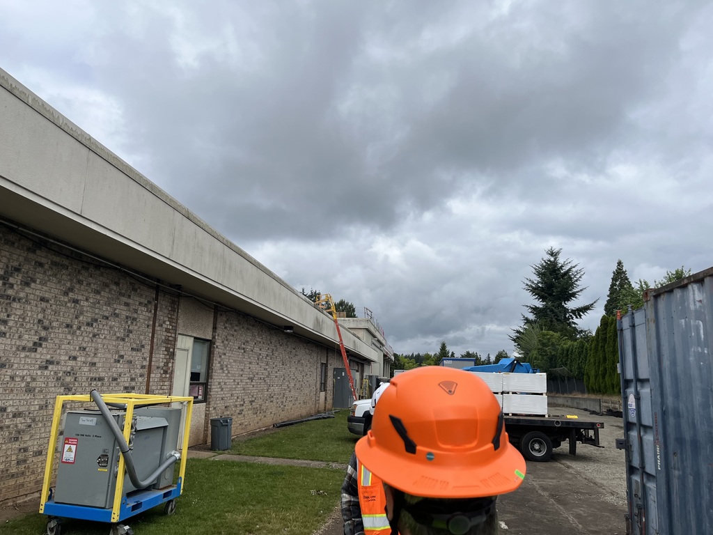 Person wearing hard hat looking at a ladder going onto a roof.