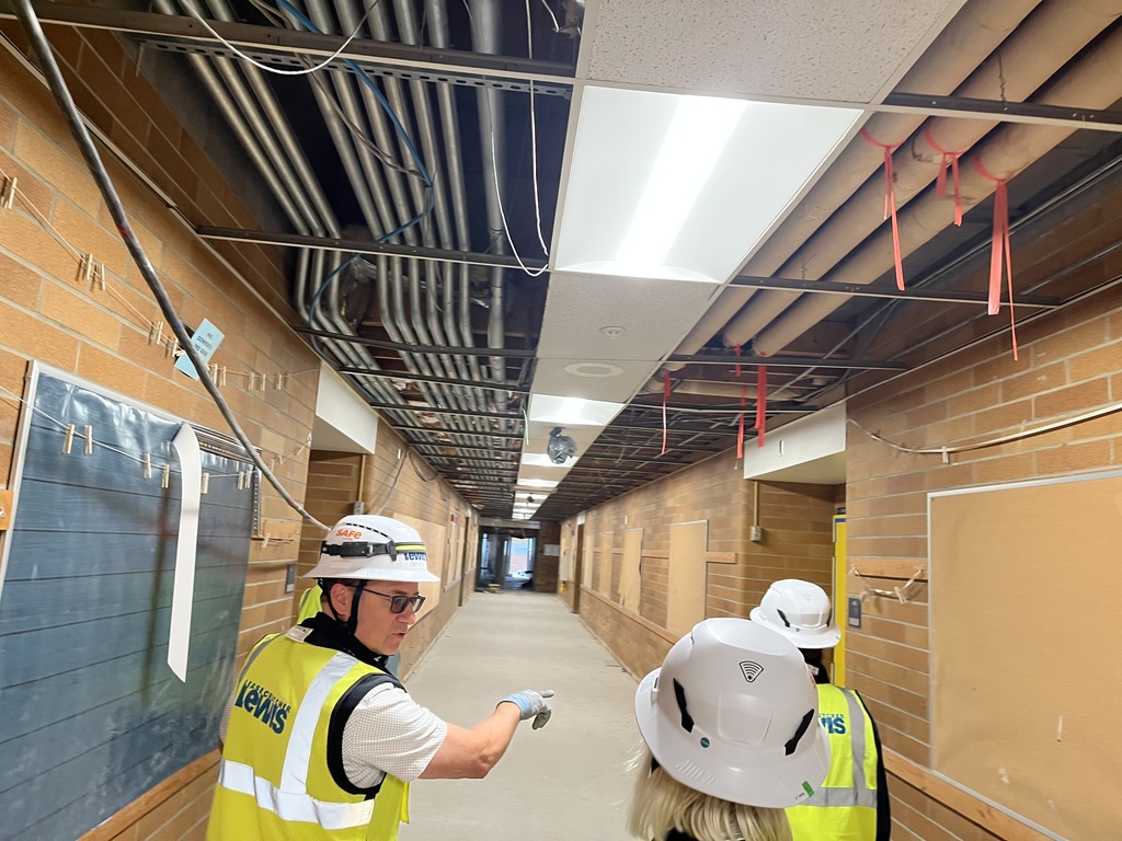 Three people wearing hard hats walking down a hallway that is under construction.