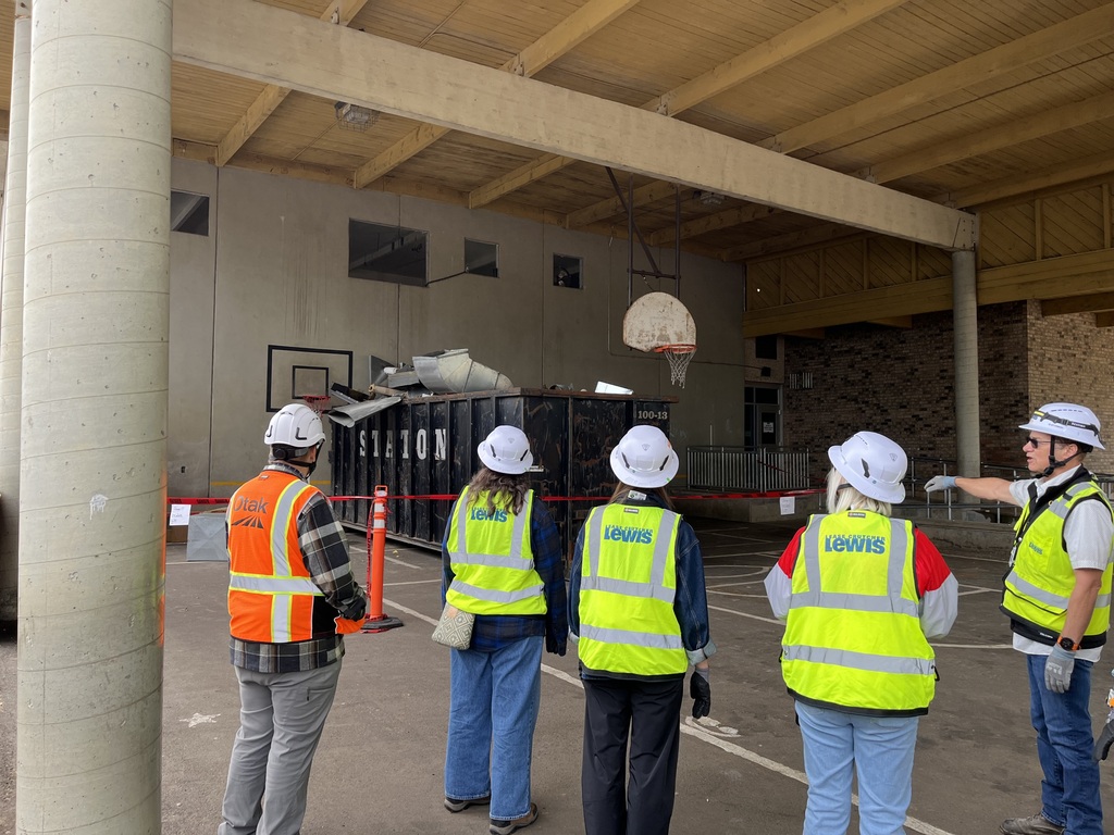5 people wearing hard hats standing outside looking at a dumpster of construction materials .