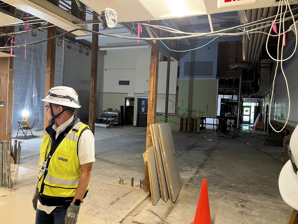 Person wearing a hard hat stadning in a large room that is under construction.