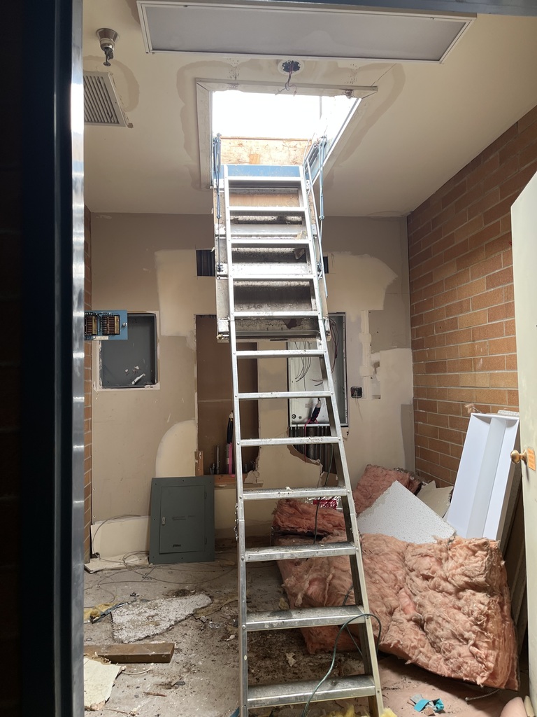 Ladder going to a daylight opening in the roof in a room that is under construction. 