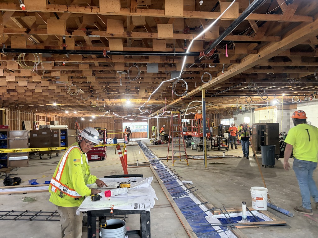 Large room under construction with many construction workers working and wearing hard hats.