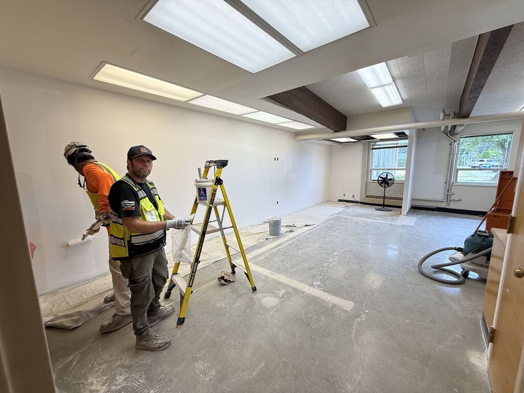Room with two construction workers working and a ladder.
