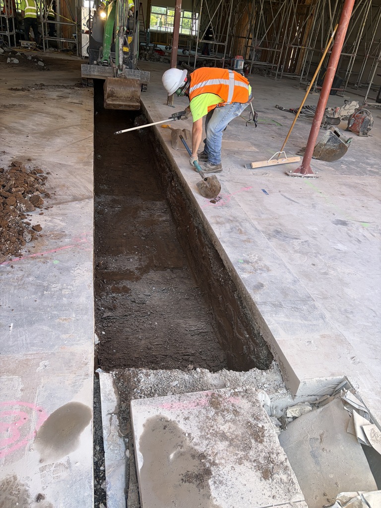 A person wearing construction gear measuring part of the floor that has been removed in an area that is under construction.