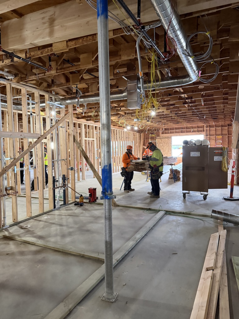 People in construction gear working in a room with wood framing.