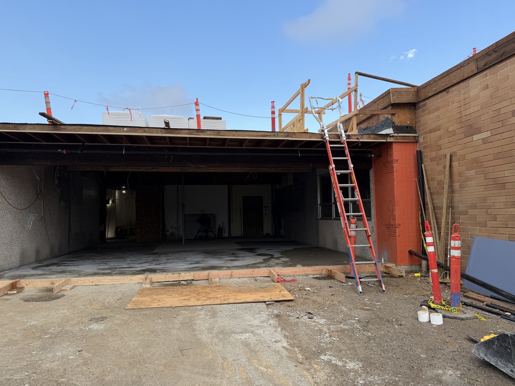 Outside of the building with a ladder going onto the roof with orange cones.