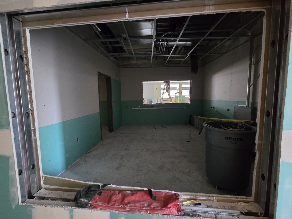 A window frame looking into a new classroom area that is under construction. A person is on the ladder in the background.