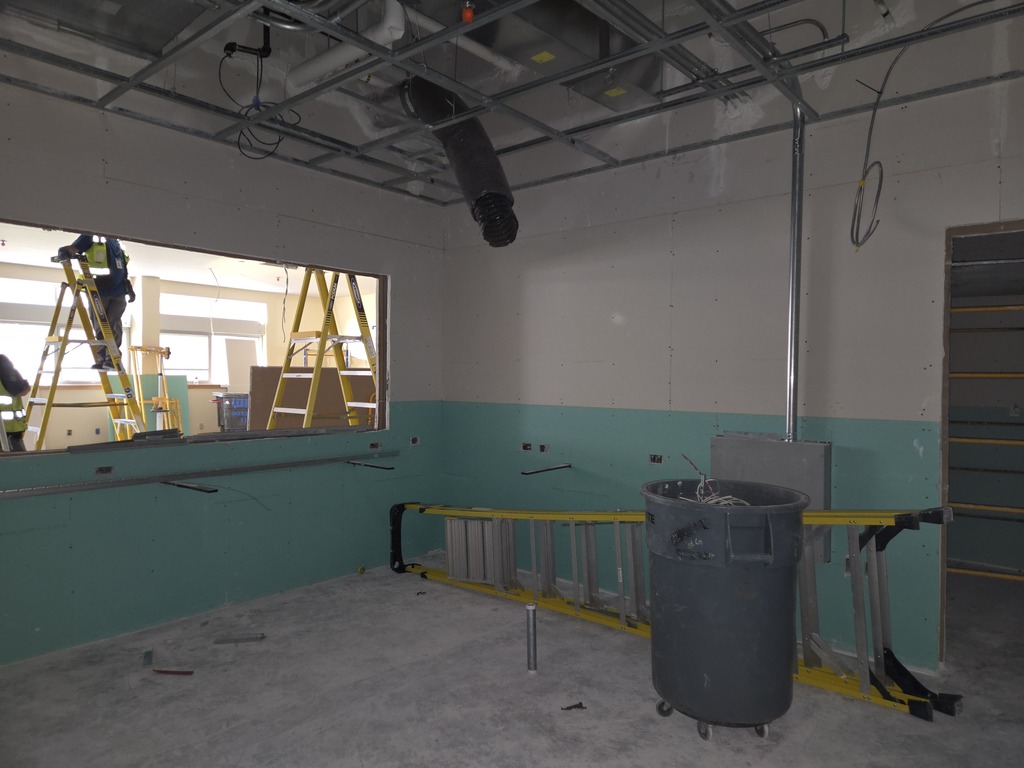A room under with a man standing on a ladder in the backgrounf and some construction equipment.