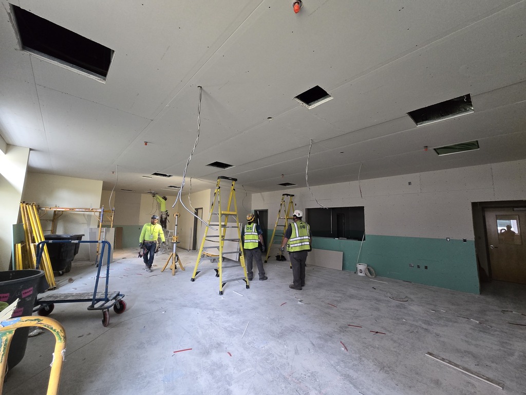 A room under construction with three people and two yellow ladders. Wires are hanging from the ceiling.