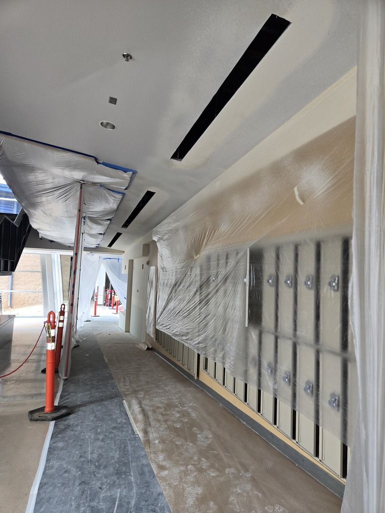 A hallway under construction with plastic covering existing lockers and orange cones.
