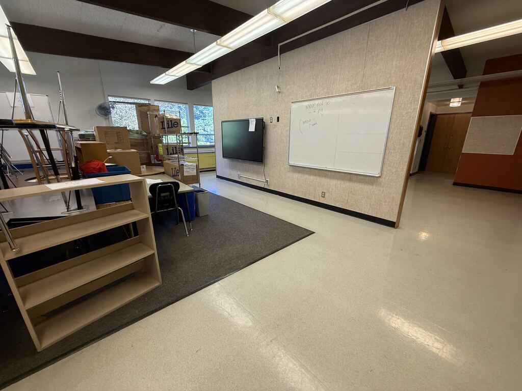 A classroom with furniture being stored and a white board and monitor hanging on the wall.